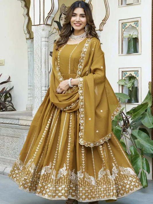 Woman wearing a mustard yellow traditional outfit with white embroidery in an indoor setting.
