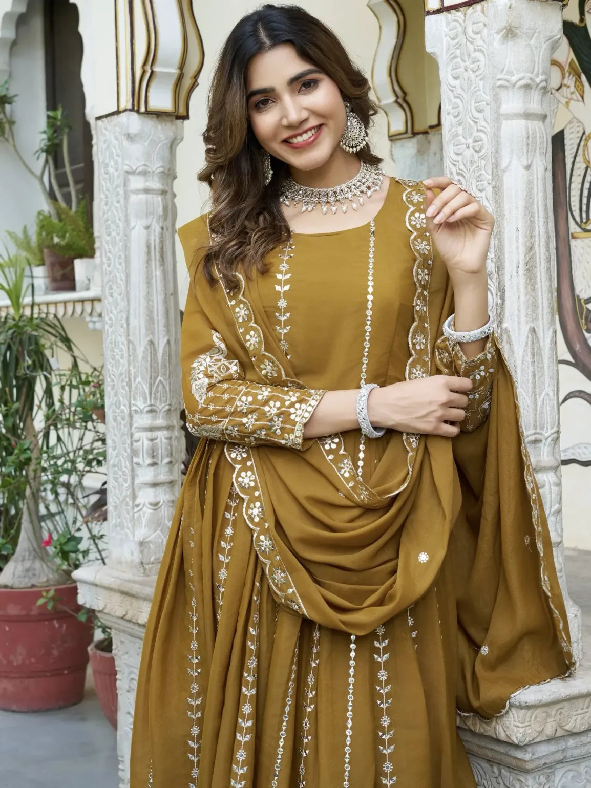 Woman in a mustard yellow traditional outfit with intricate designs, standing in an outdoor setting.