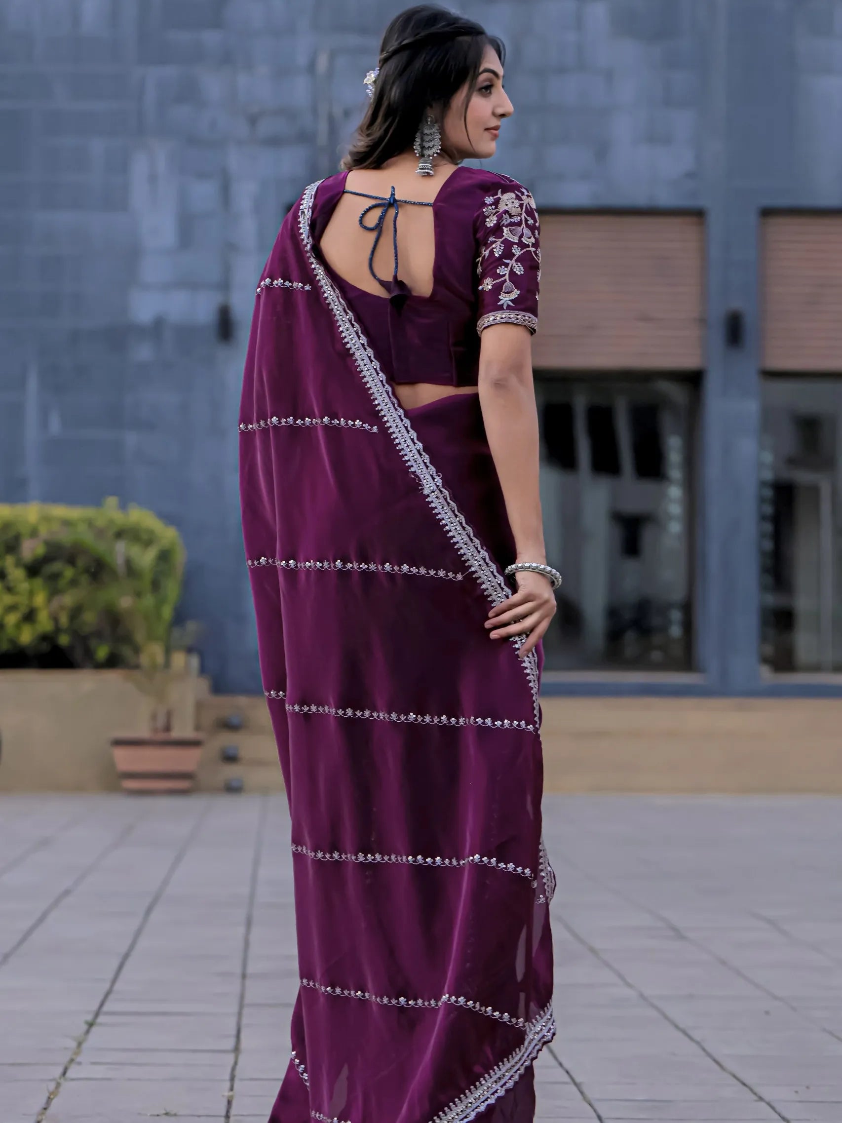 Woman wearing a purple saree with white patterns in an outdoor setting.