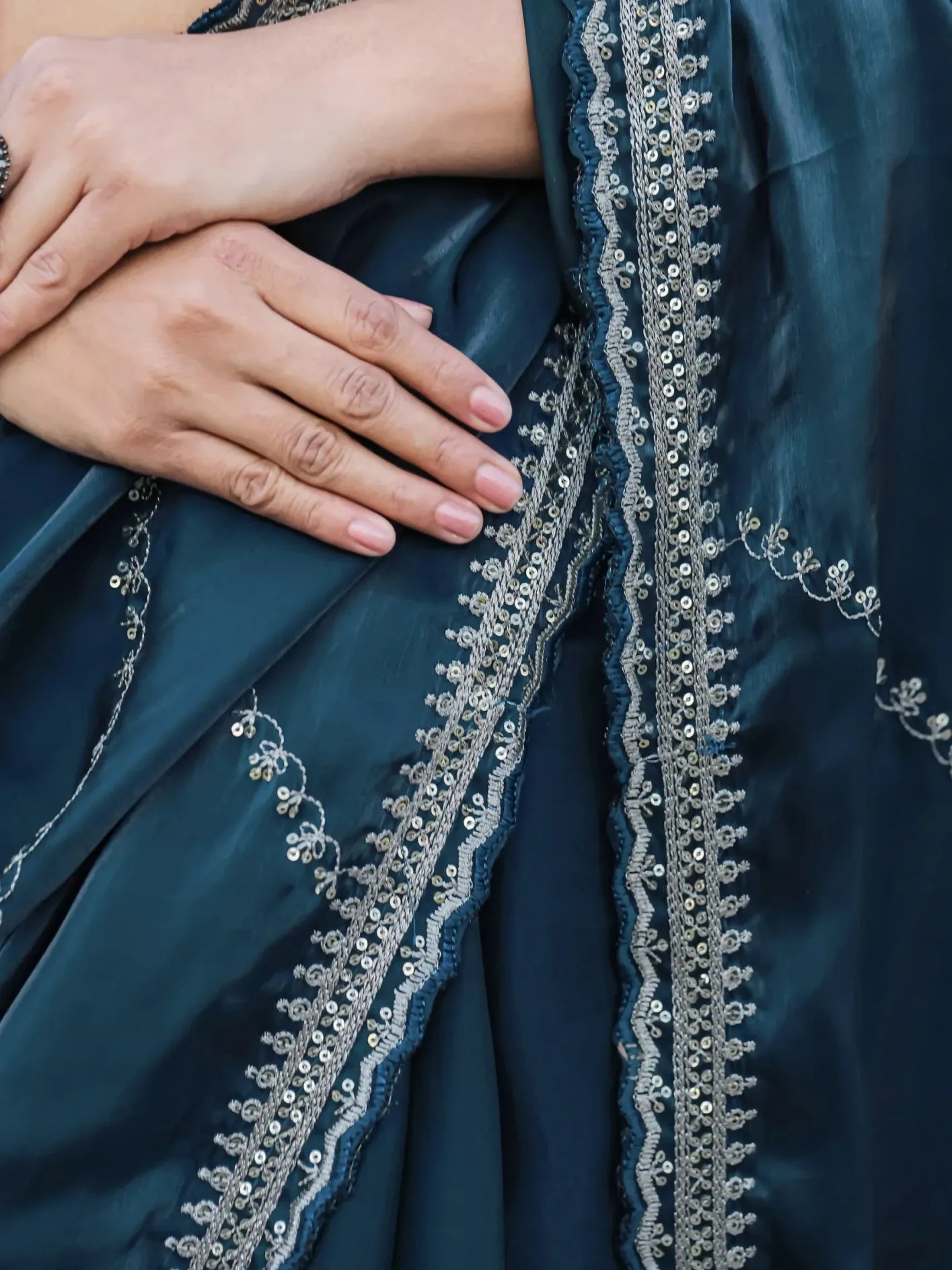 Navy blue fabric with intricate silver embroidery and a hand holding it.