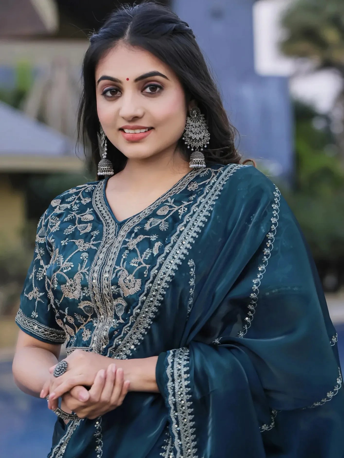 Woman wearing a teal embroidered saree with a blurred outdoor background