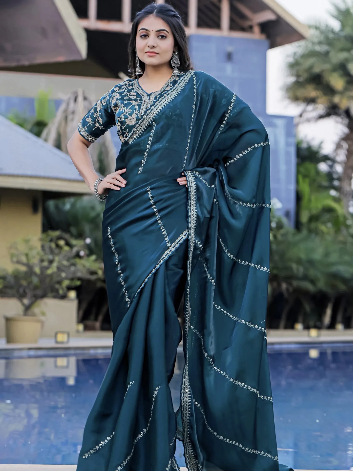 Woman wearing a teal saree with a pool and building in the background