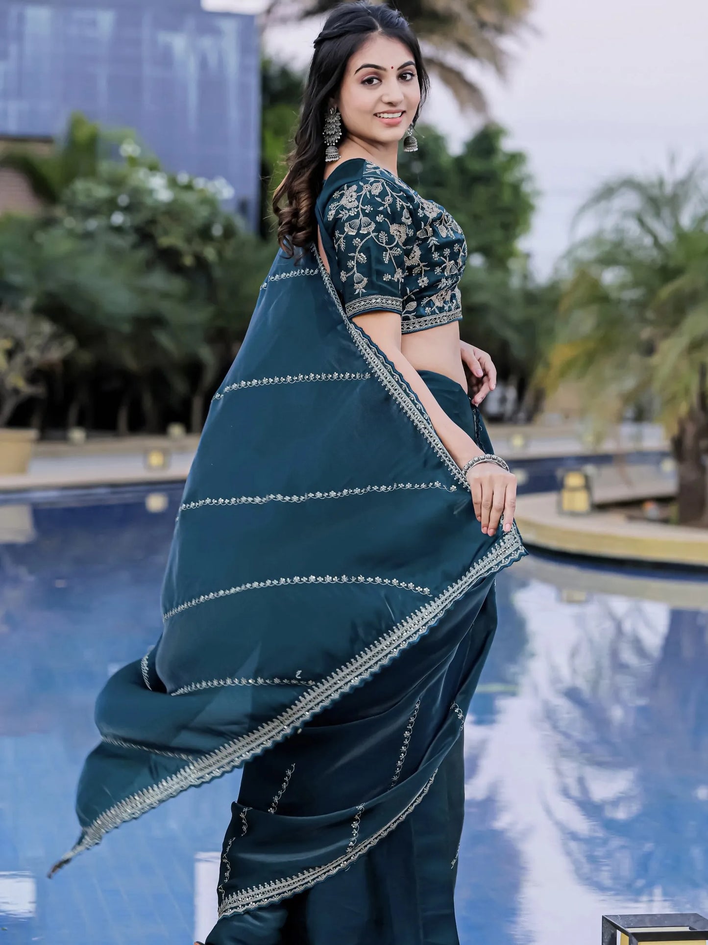 Woman in a teal saree with a matching blouse by a poolside