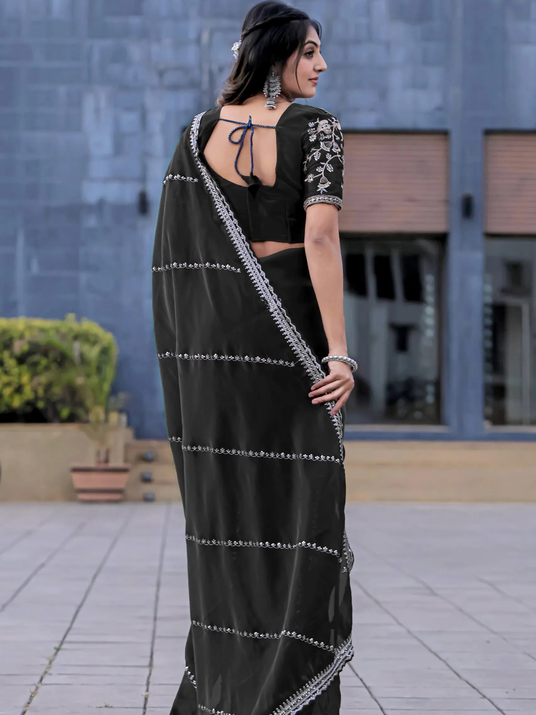 Woman wearing a black saree with white embroidery in an outdoor setting.