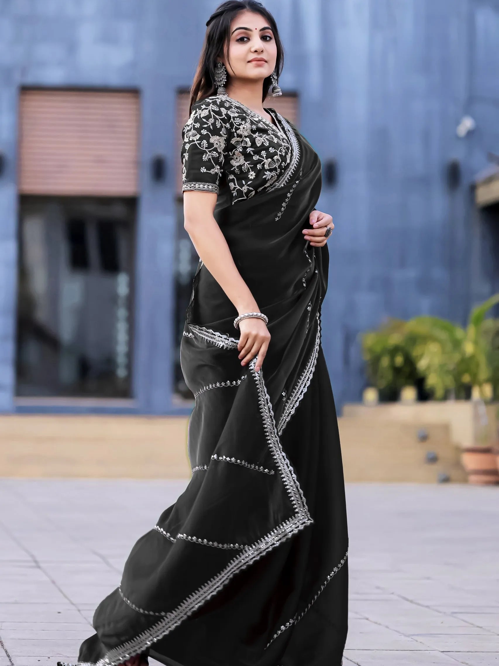 Woman wearing a black saree with silver embroidery outdoors.