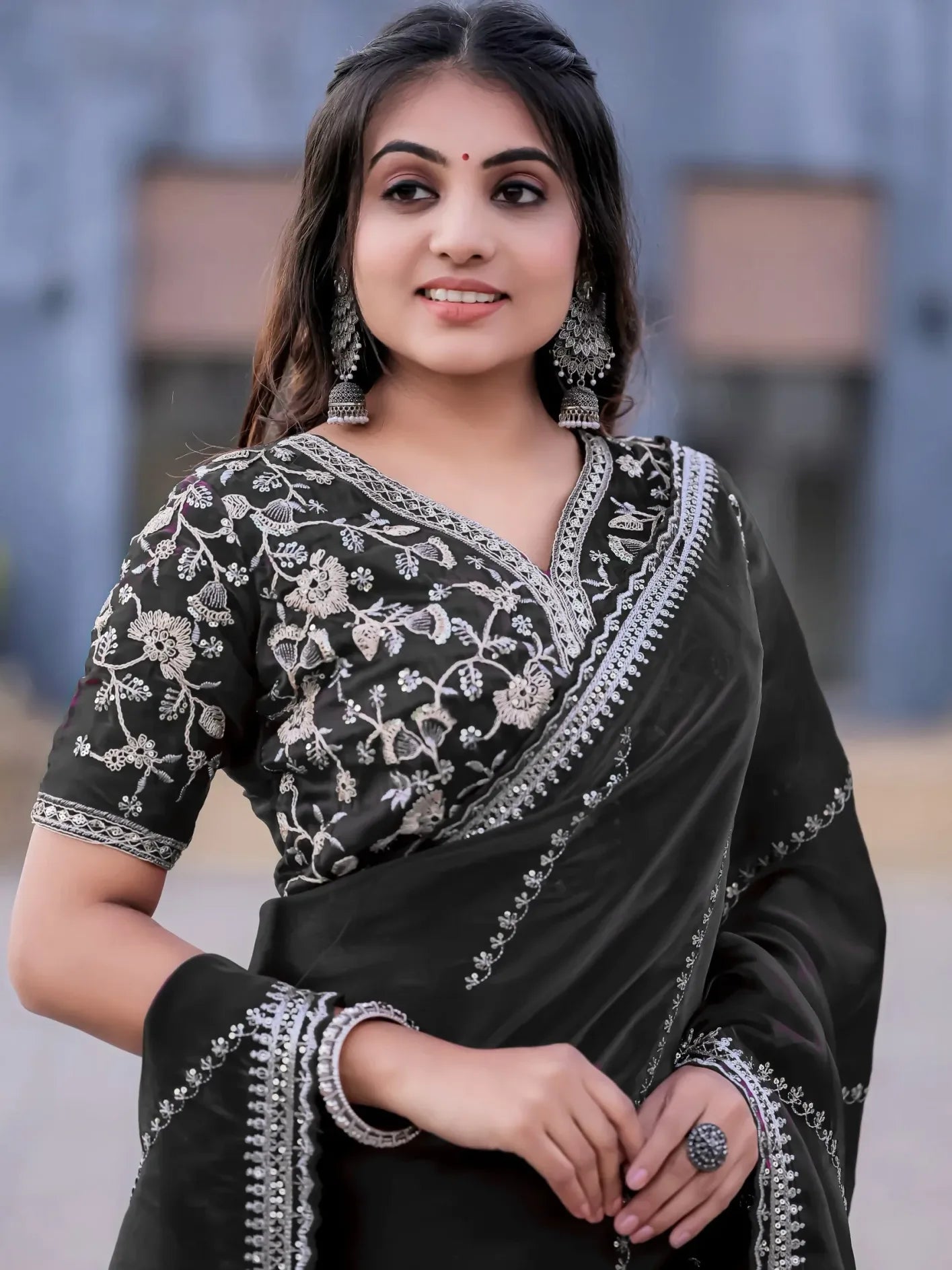 Woman wearing a black saree with white embroidery against a blurred background