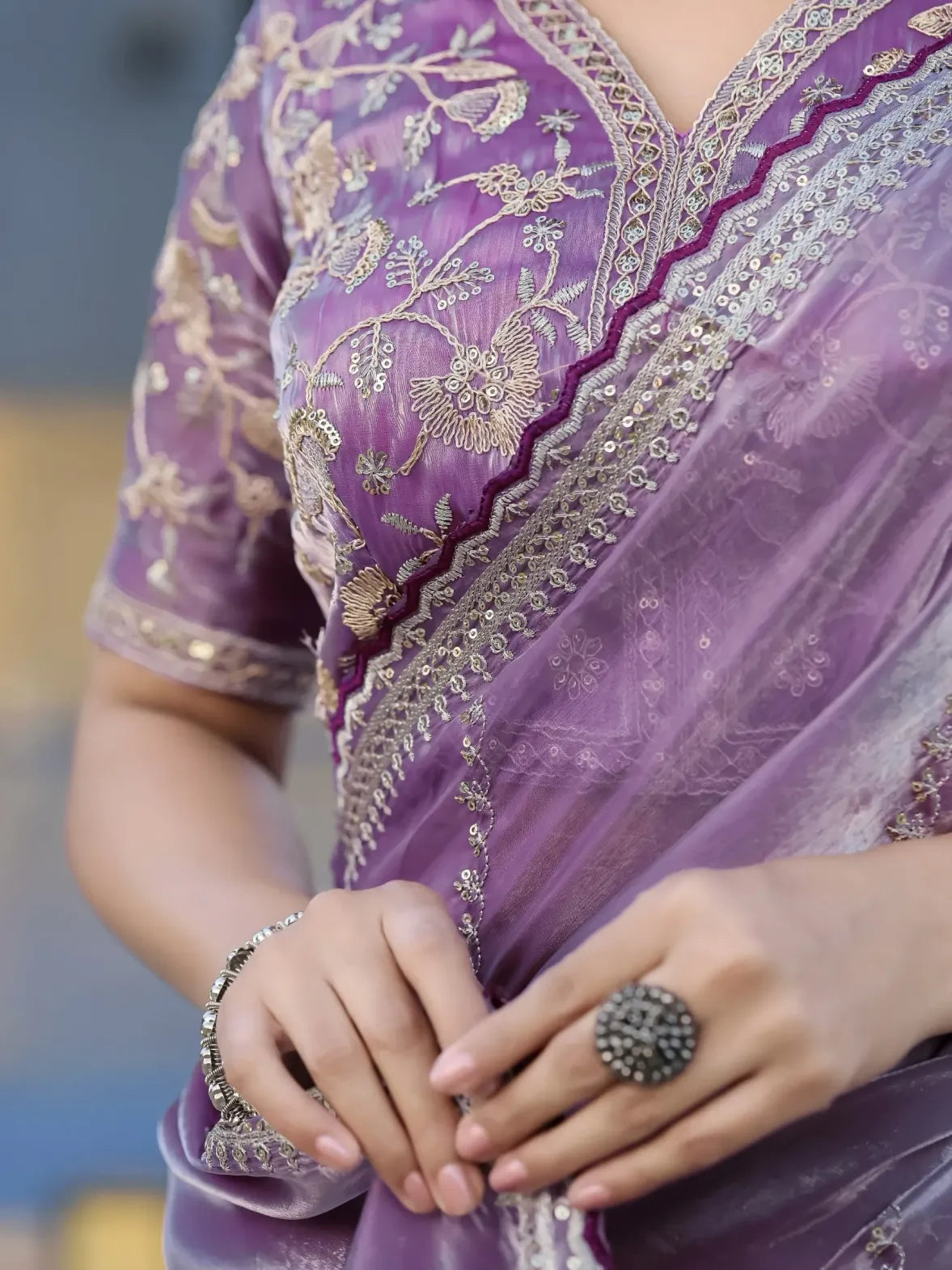 Close-up of a purple saree with intricate gold embroidery, held by a person.