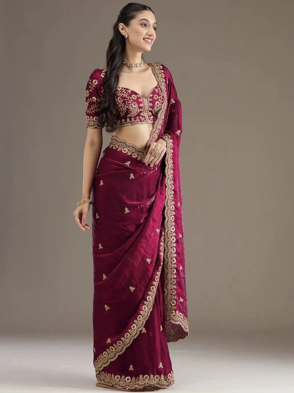 Woman wearing a maroon saree with gold embroidery on a plain background