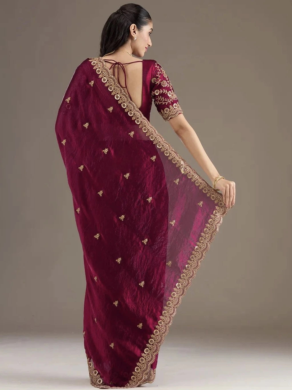 Woman wearing a maroon saree with gold embroidery on a plain background