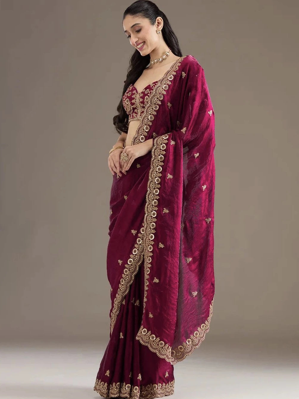 Woman wearing a maroon saree with gold embroidery on a plain background