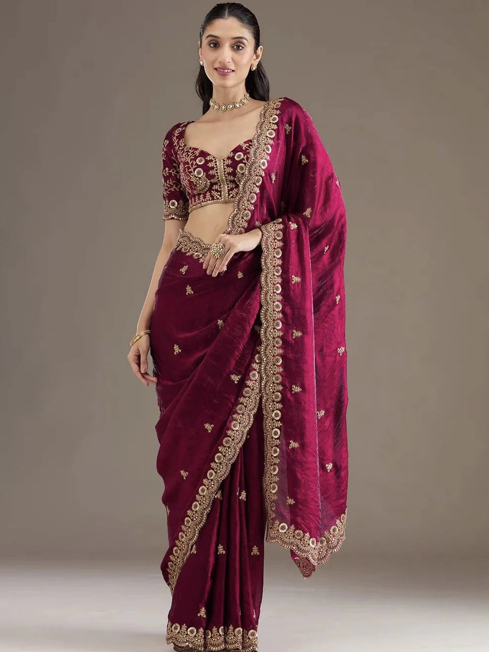 Woman wearing a maroon saree with gold embroidery against a neutral background