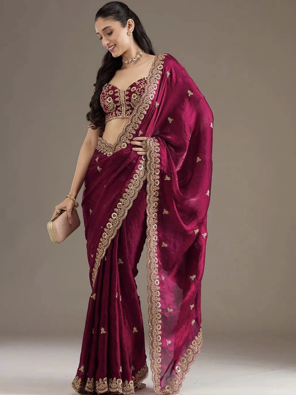 Woman wearing a maroon saree with gold embroidery against a plain background