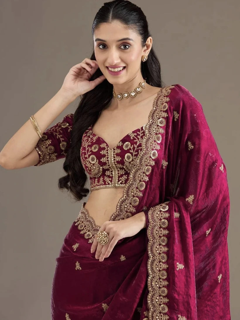 Woman wearing a maroon saree with gold embroidery against a neutral background