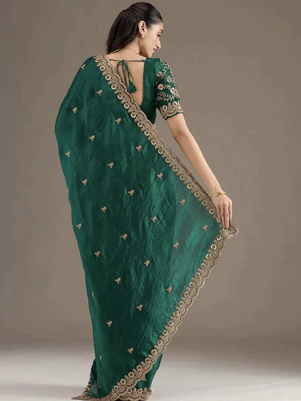 Woman wearing a green saree with gold embroidery on a plain background