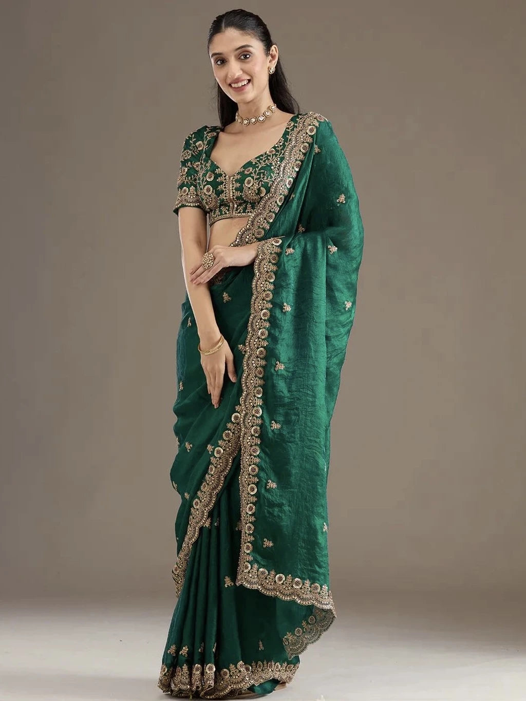 Woman wearing a green saree with gold embroidery on a plain background