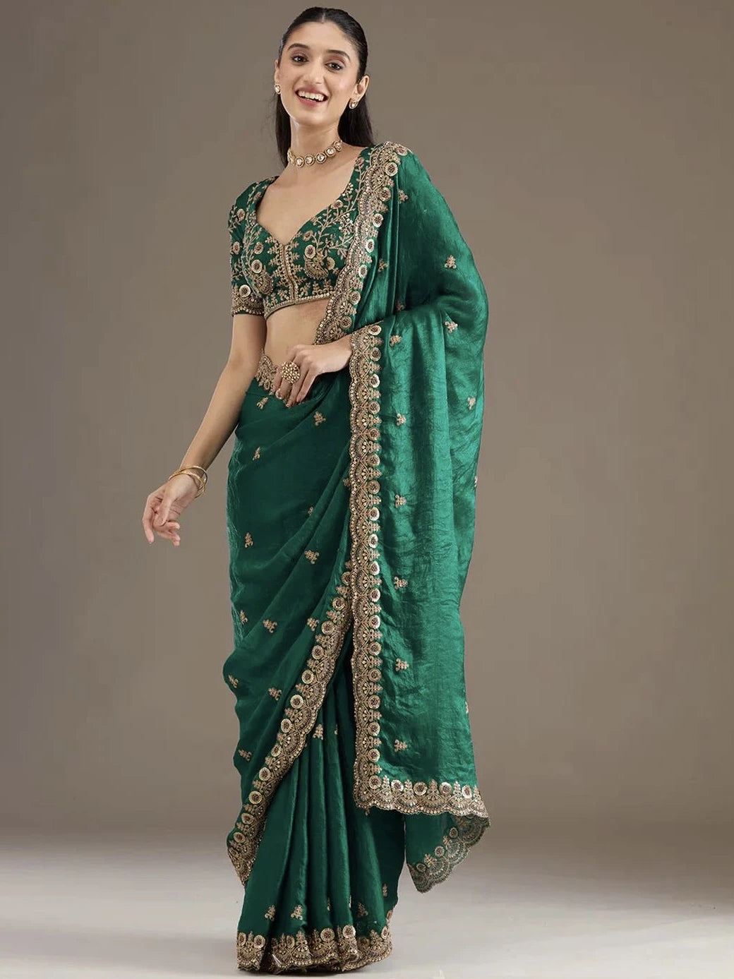 Woman wearing a green saree with gold embroidery on a plain background