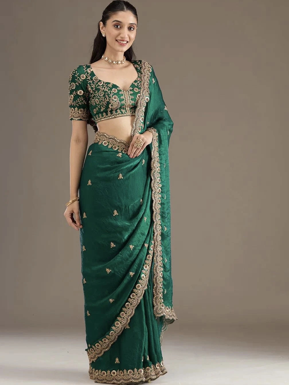 Woman wearing a green saree with gold embroidery on a plain background
