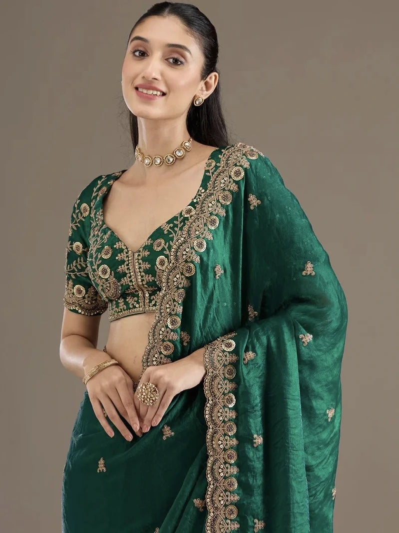 Woman wearing a green saree with gold embroidery on a plain background