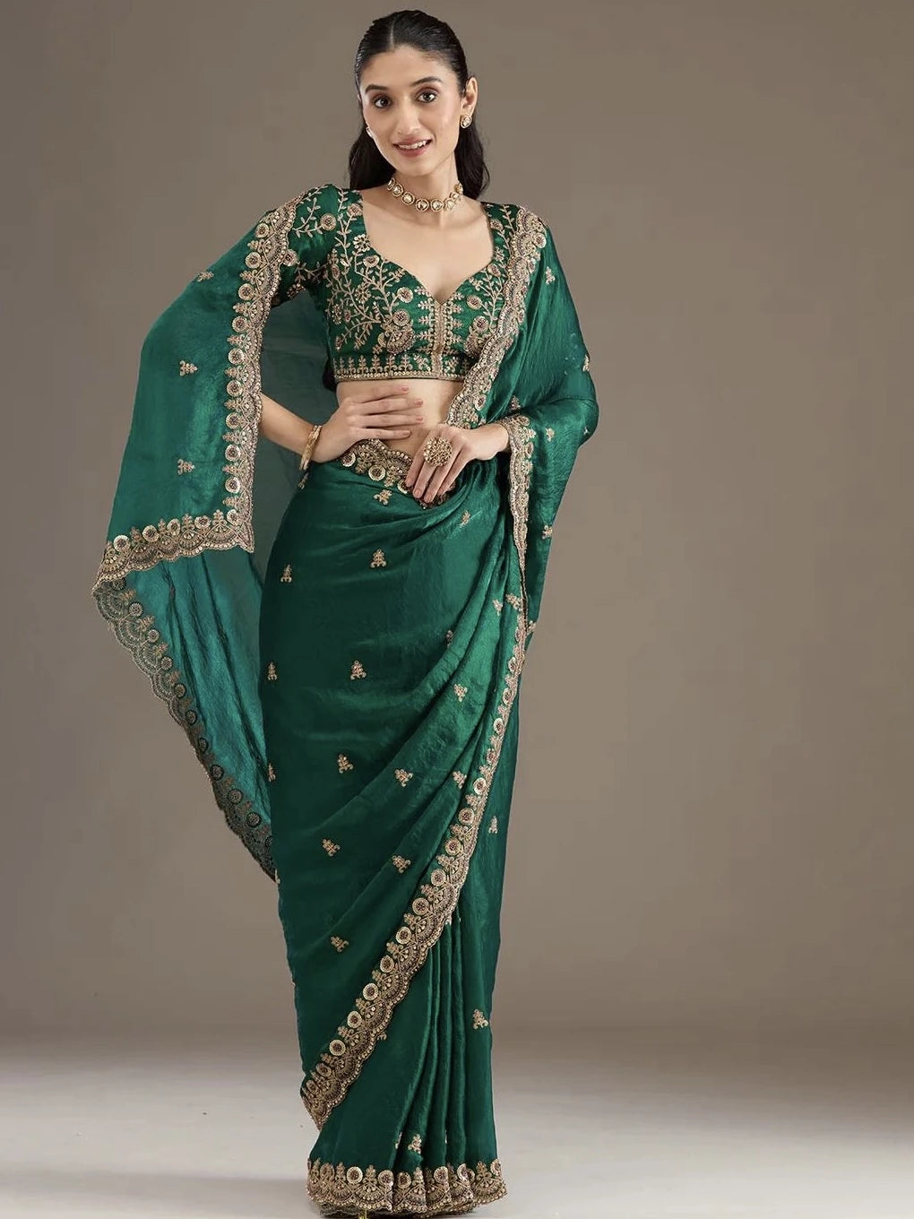 Woman wearing a green saree with gold embroidery on a plain background