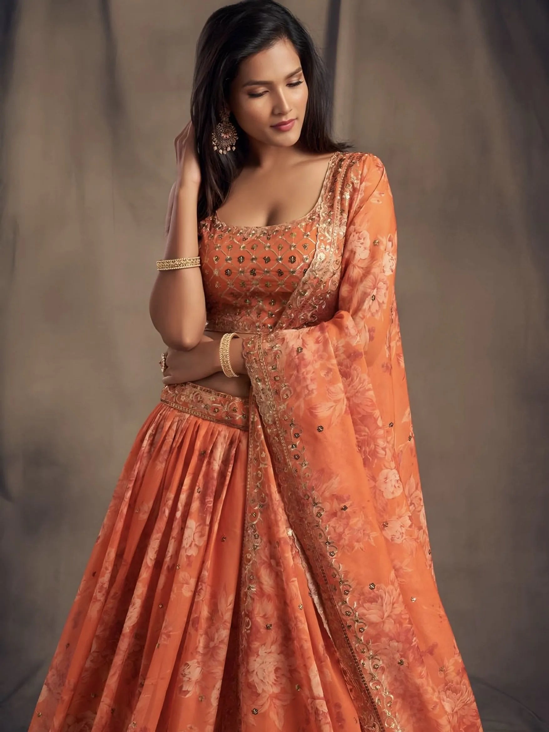 Woman wearing an orange traditional outfit with intricate patterns against a neutral background