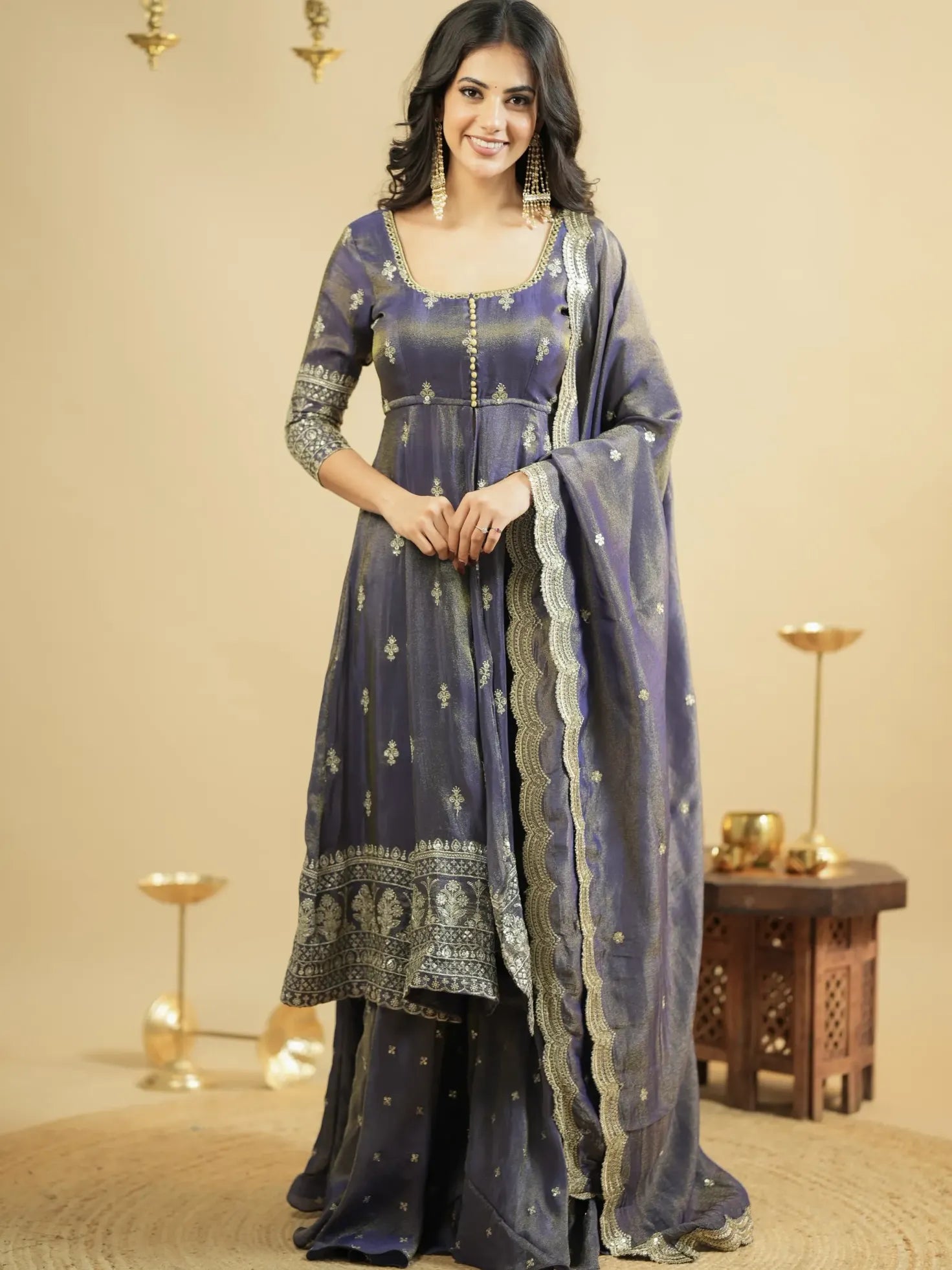 Woman wearing a traditional outfit with a blue and silver patterned dress and dupatta against a beige background.