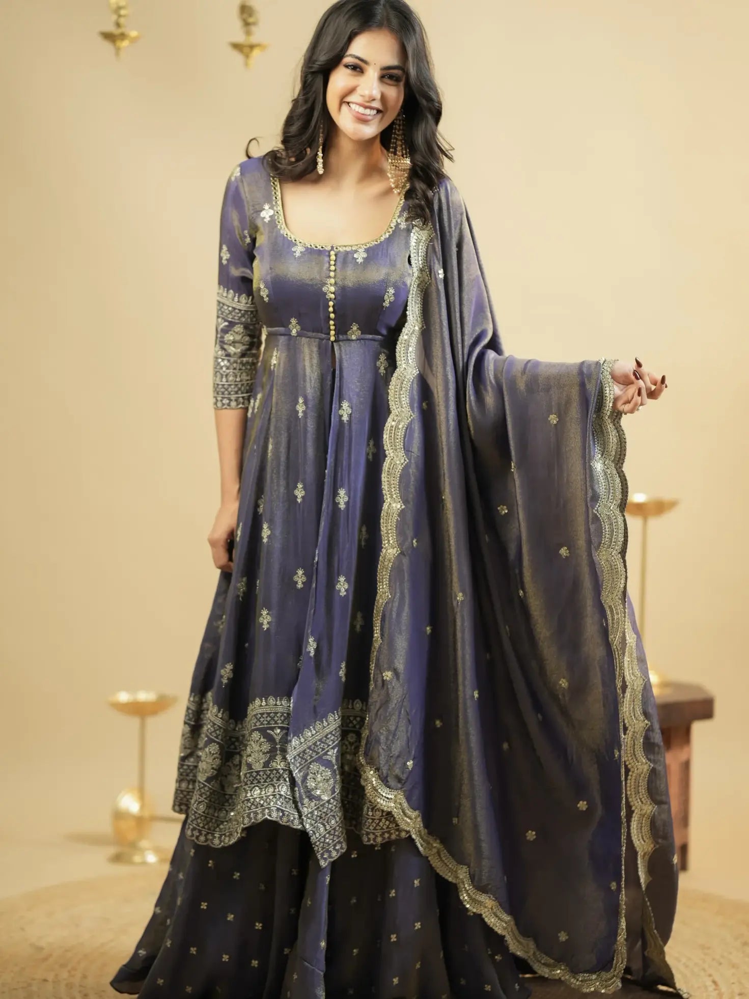 Woman wearing a traditional outfit with a blue and gold dress and dupatta against a beige background