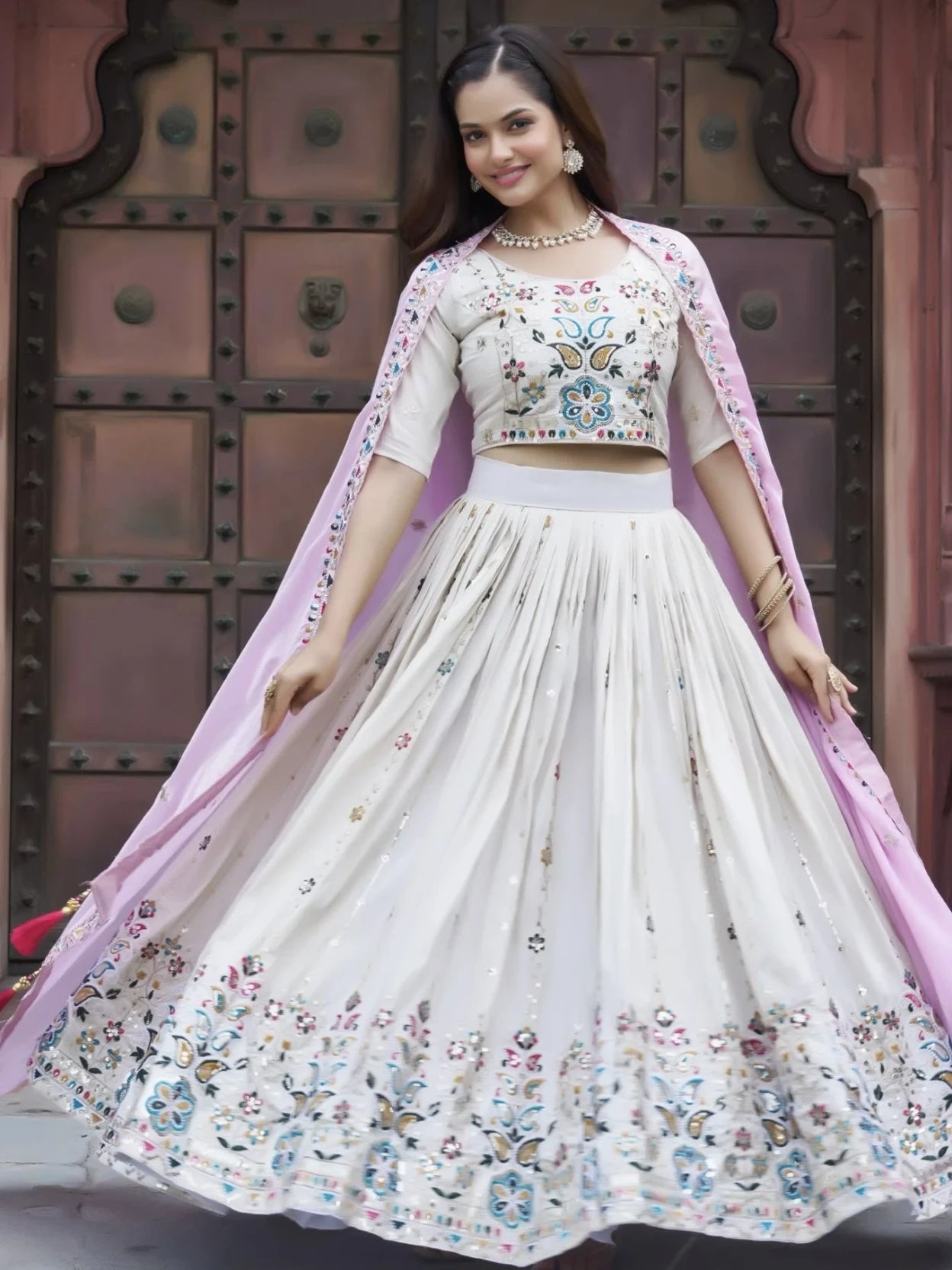 Woman in a traditional outfit with floral patterns in front of a decorative door.