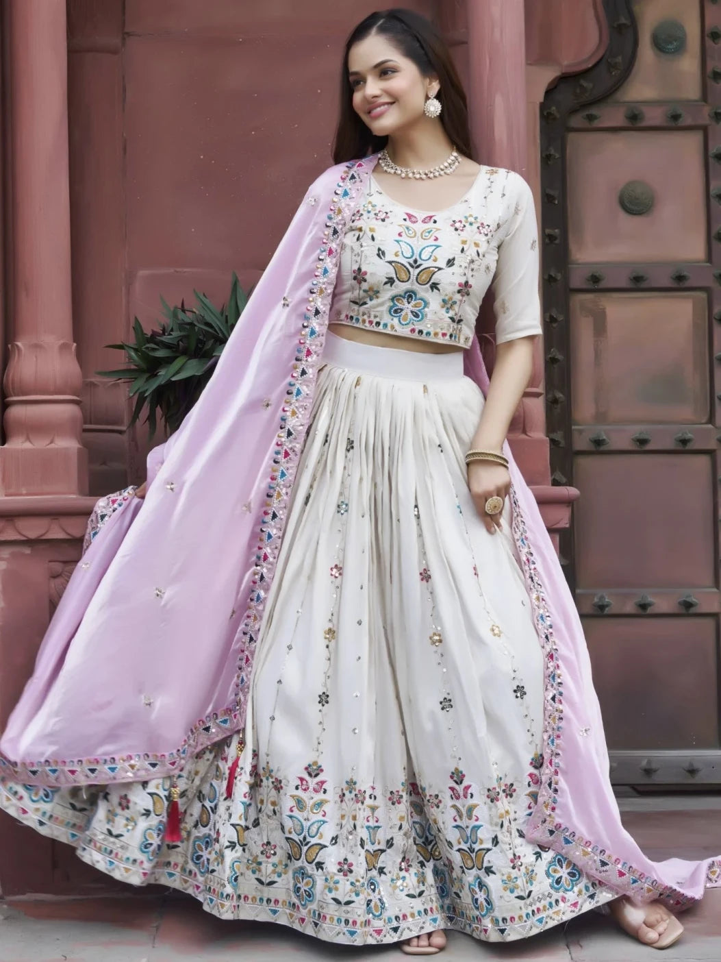 Woman in traditional outfit with floral patterns standing in front of a textured wall.