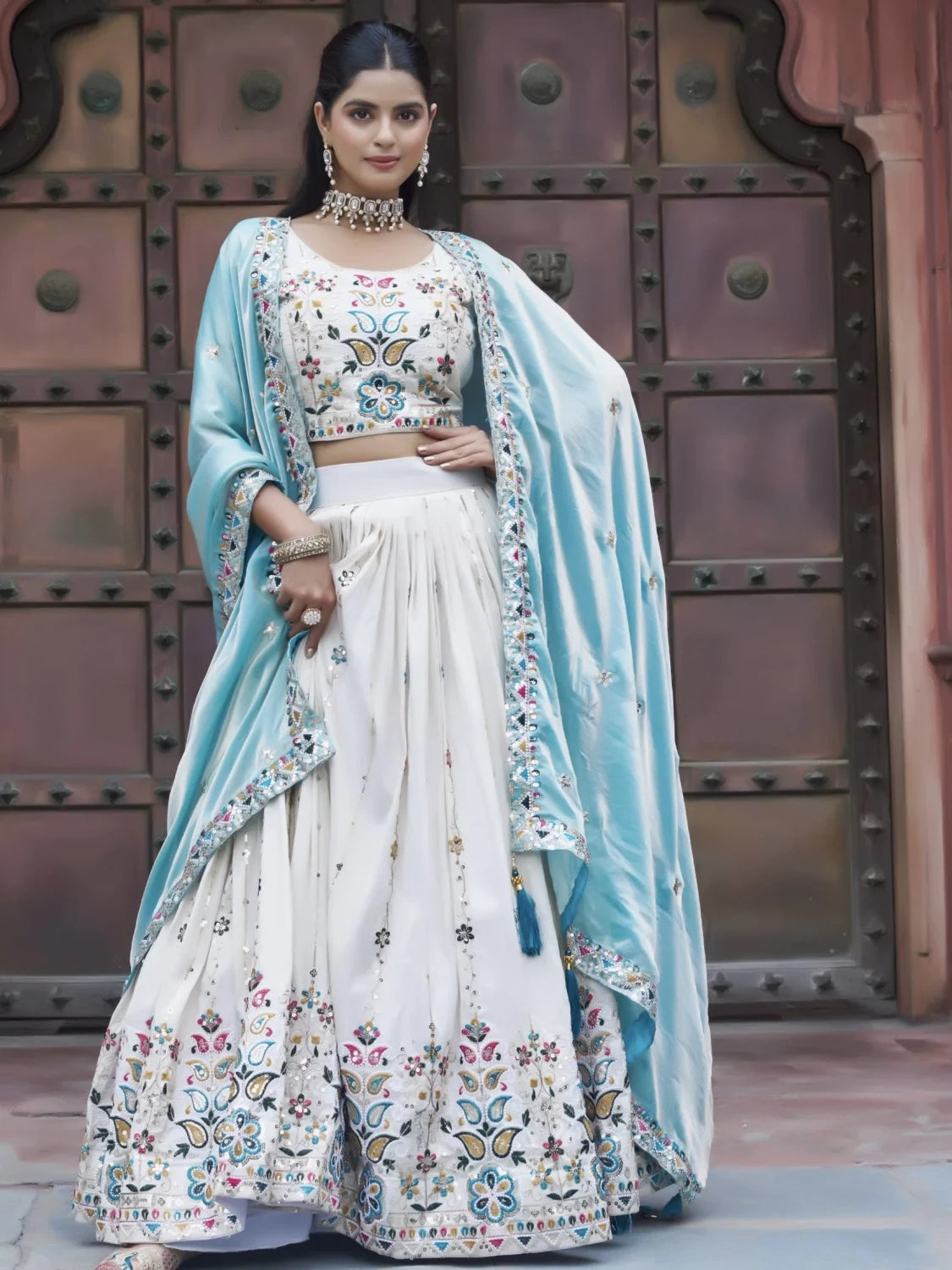 Woman in a traditional outfit with a floral design in front of a decorative wall.