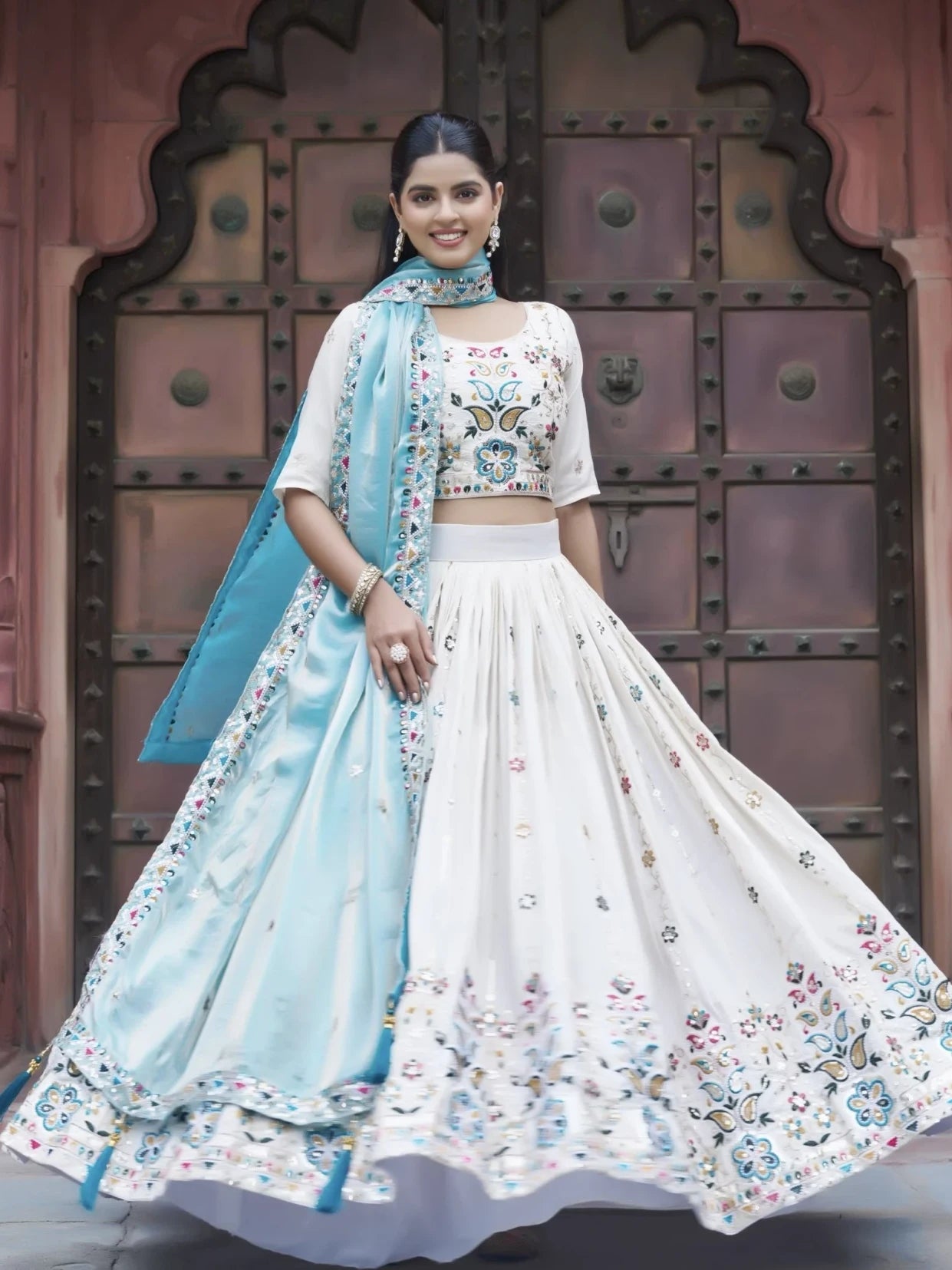 Woman in traditional outfit with floral patterns in front of a decorative door.