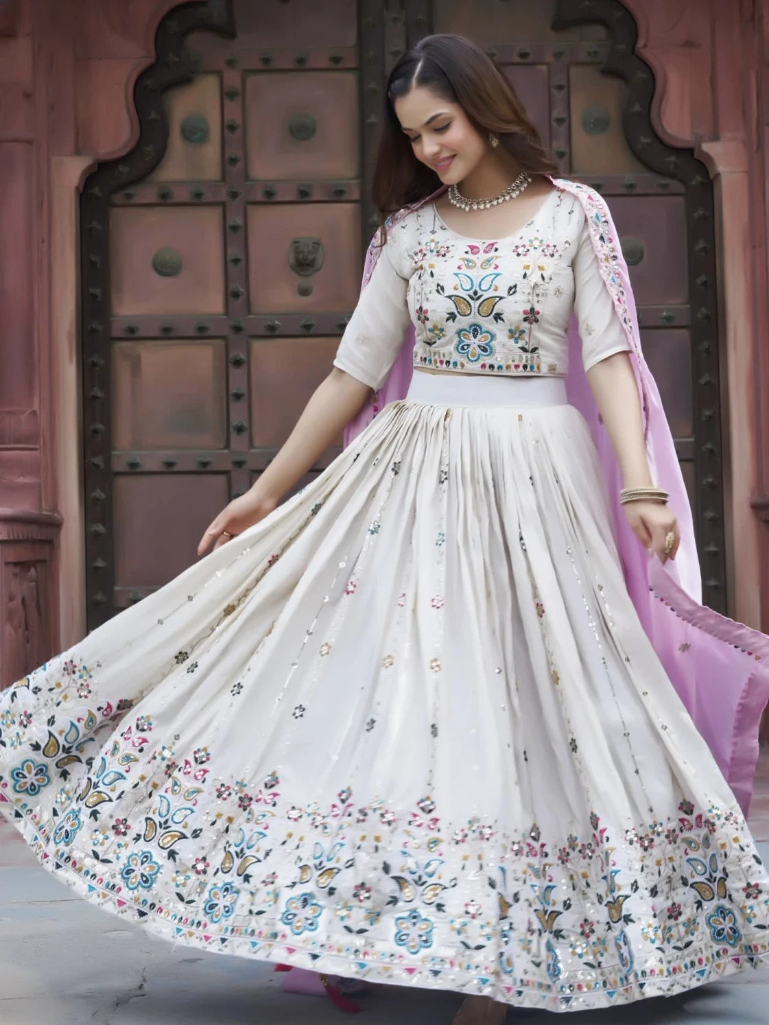 Woman wearing a traditional embroidered outfit in front of a decorative door.