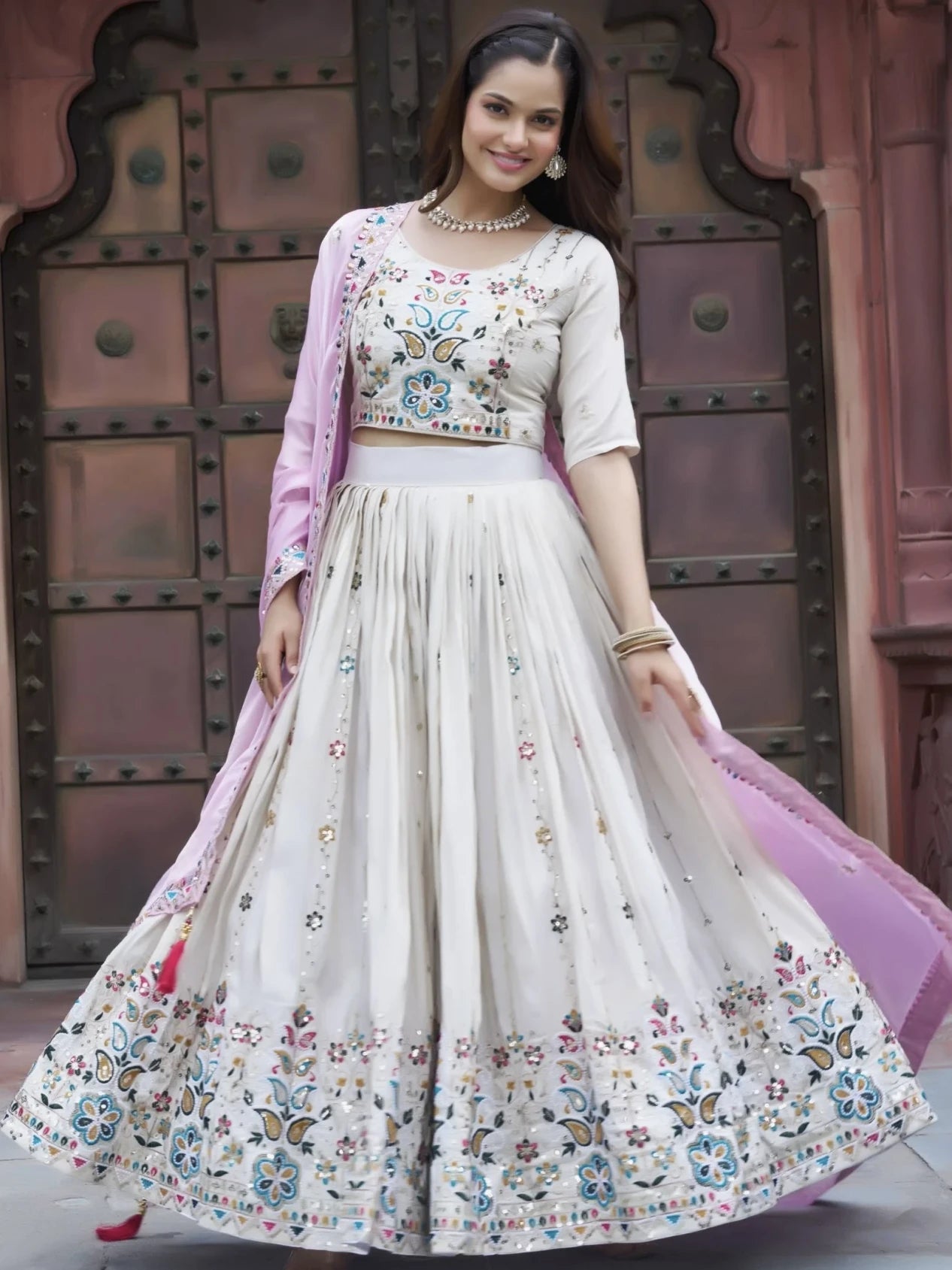 Woman in a traditional outfit with floral patterns in front of an ornate door.