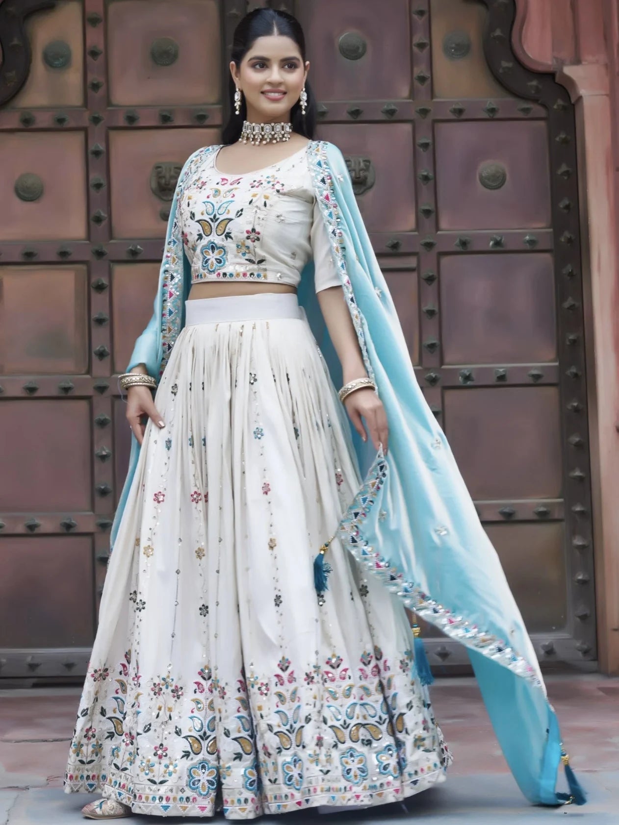 Woman in traditional outfit with floral patterns in front of a metallic gate.