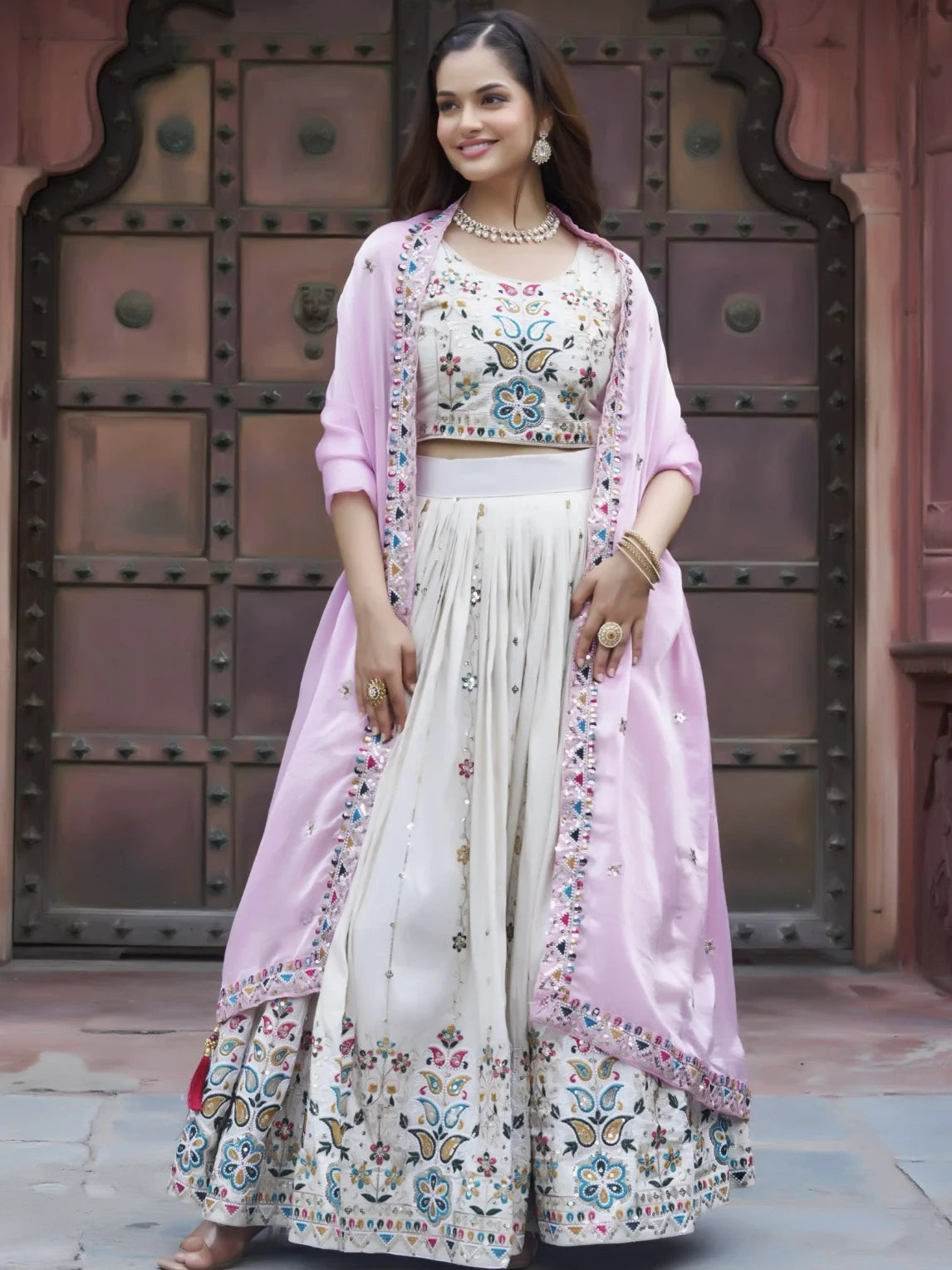 Woman in traditional outfit with floral patterns in front of a metallic gate.