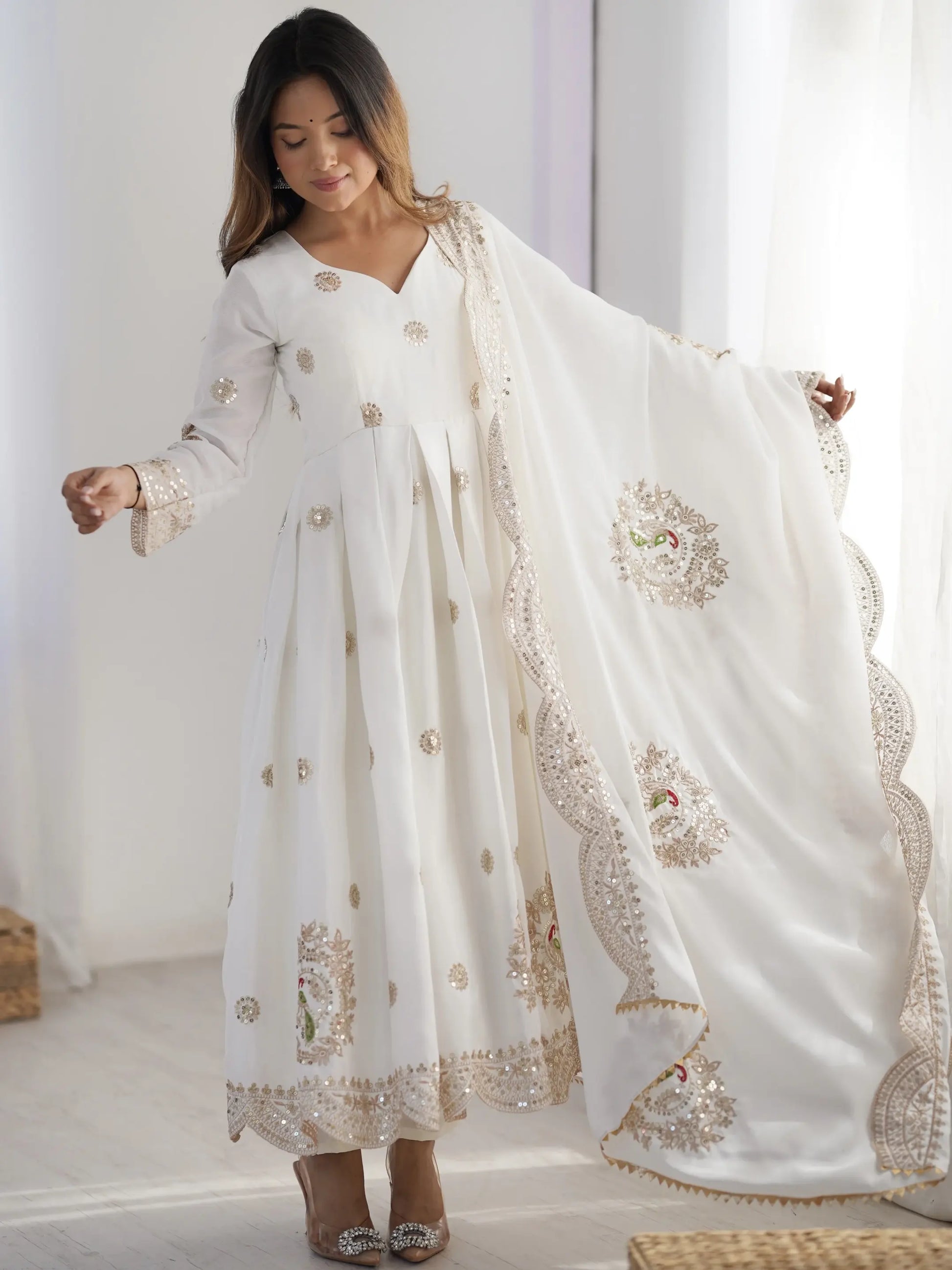 Woman wearing a white embroidered traditional outfit with a matching dupatta in a bright room.