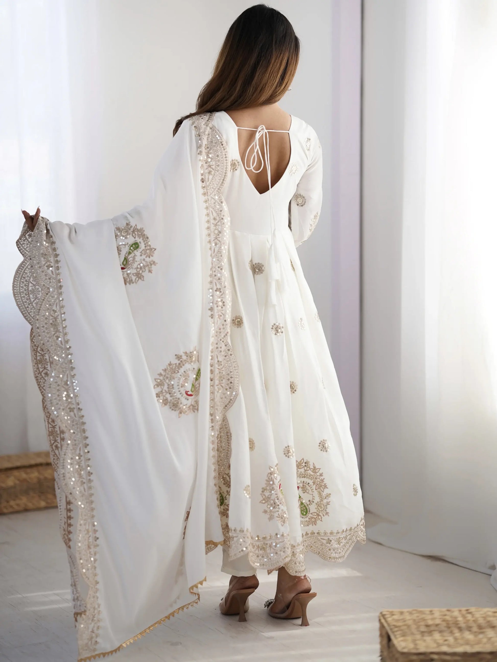 Woman wearing a white embroidered outfit with a sheer dupatta in a minimalistic setting
