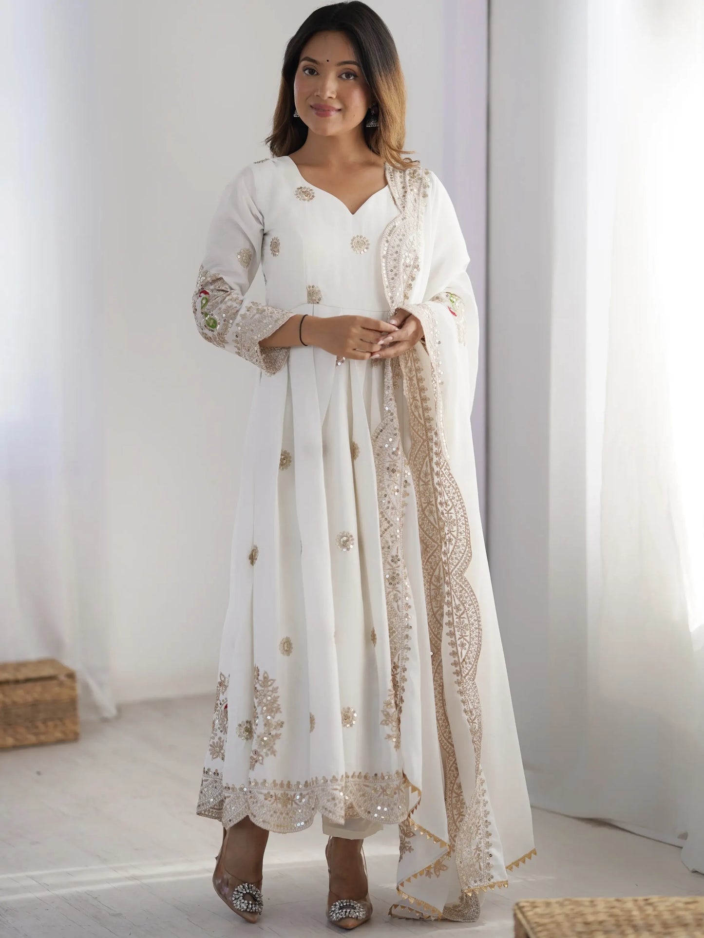 Woman wearing a white traditional outfit with gold embroidery in a minimalistic setting