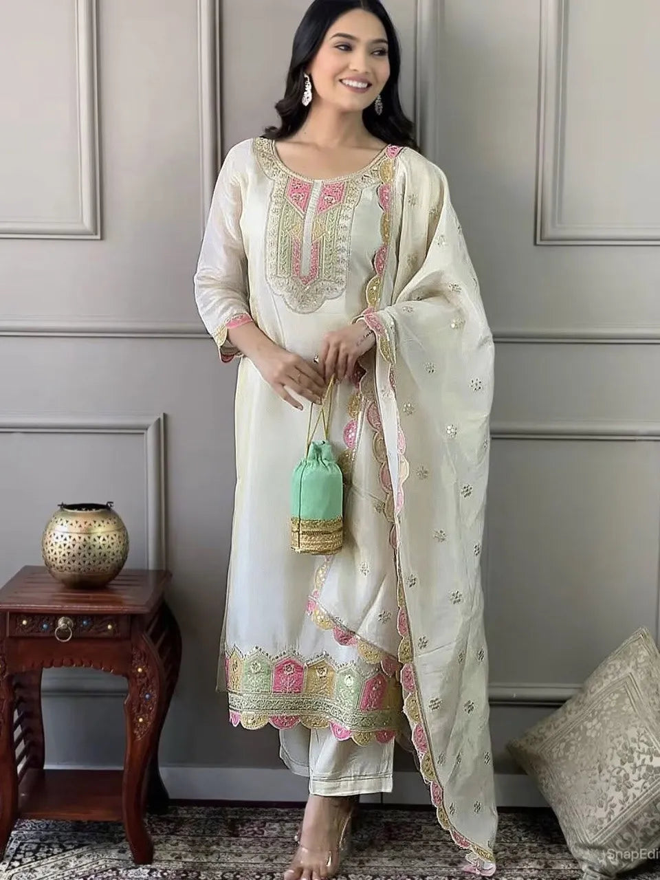Woman in a traditional outfit with embroidery, holding a green bag in a room.