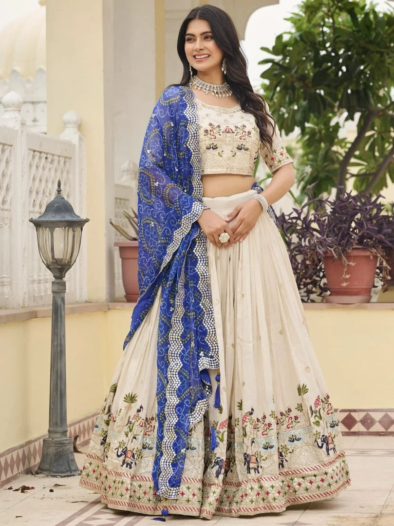 Woman in traditional embroidered outfit with blue dupatta standing outdoors.