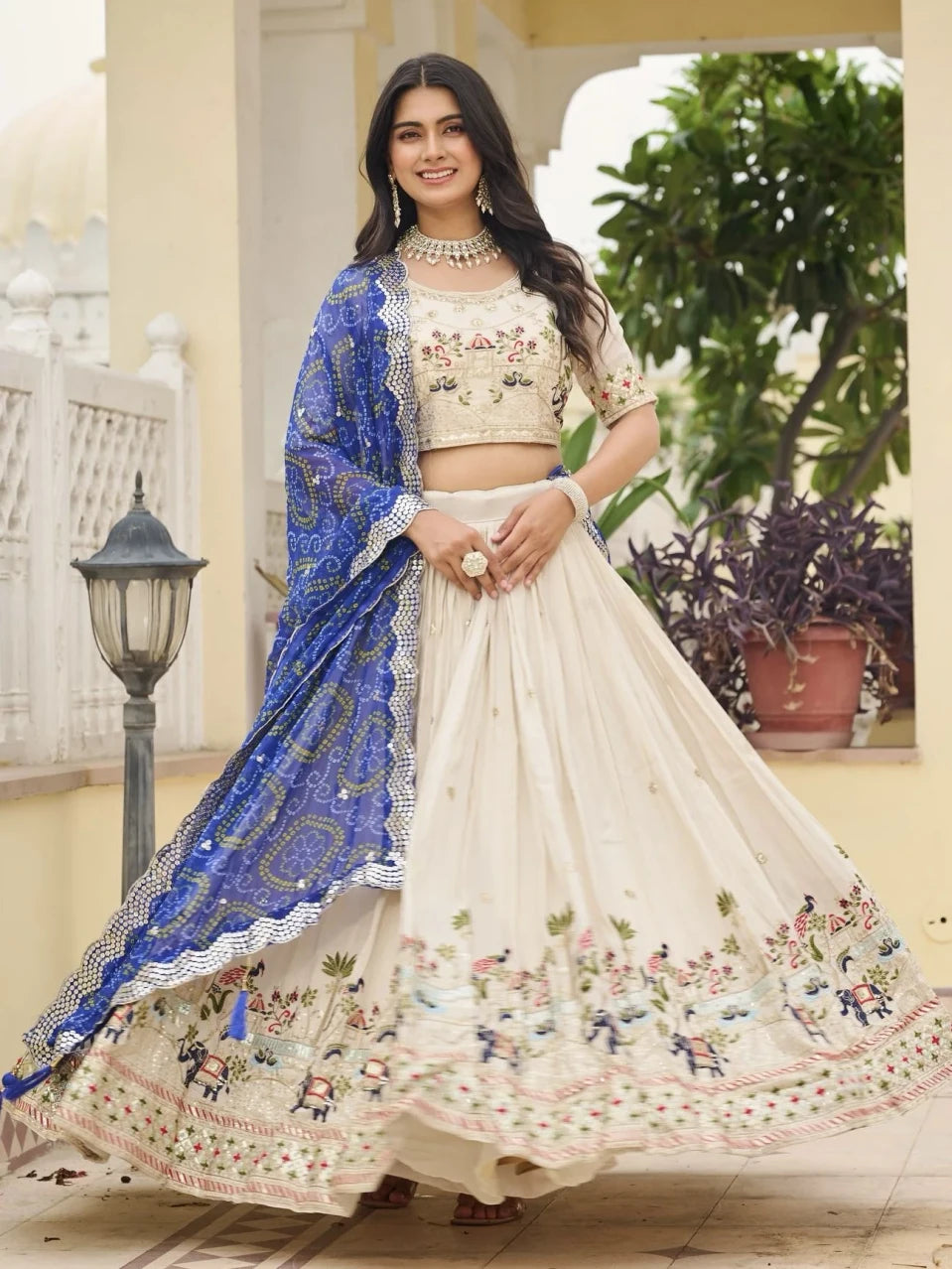 Woman in traditional embroidered outfit with blue dupatta standing outdoors.