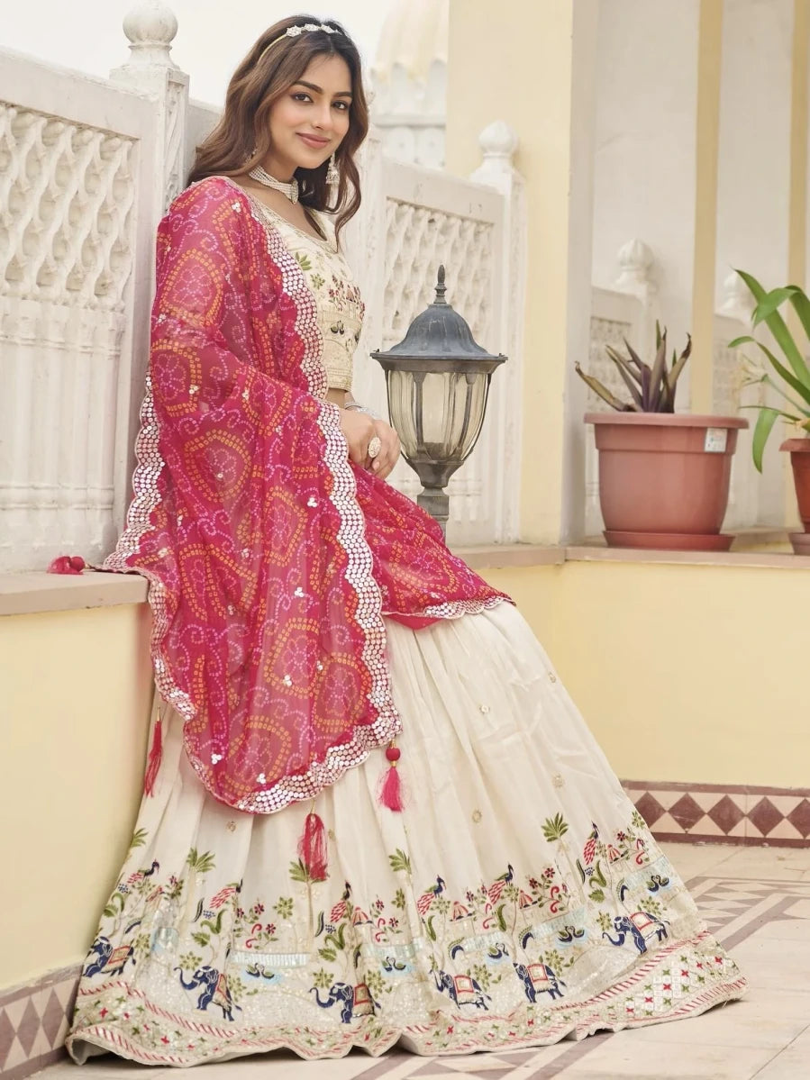 Woman in a traditional outfit with pink dupatta and white dress with floral patterns, standing on a balcony.