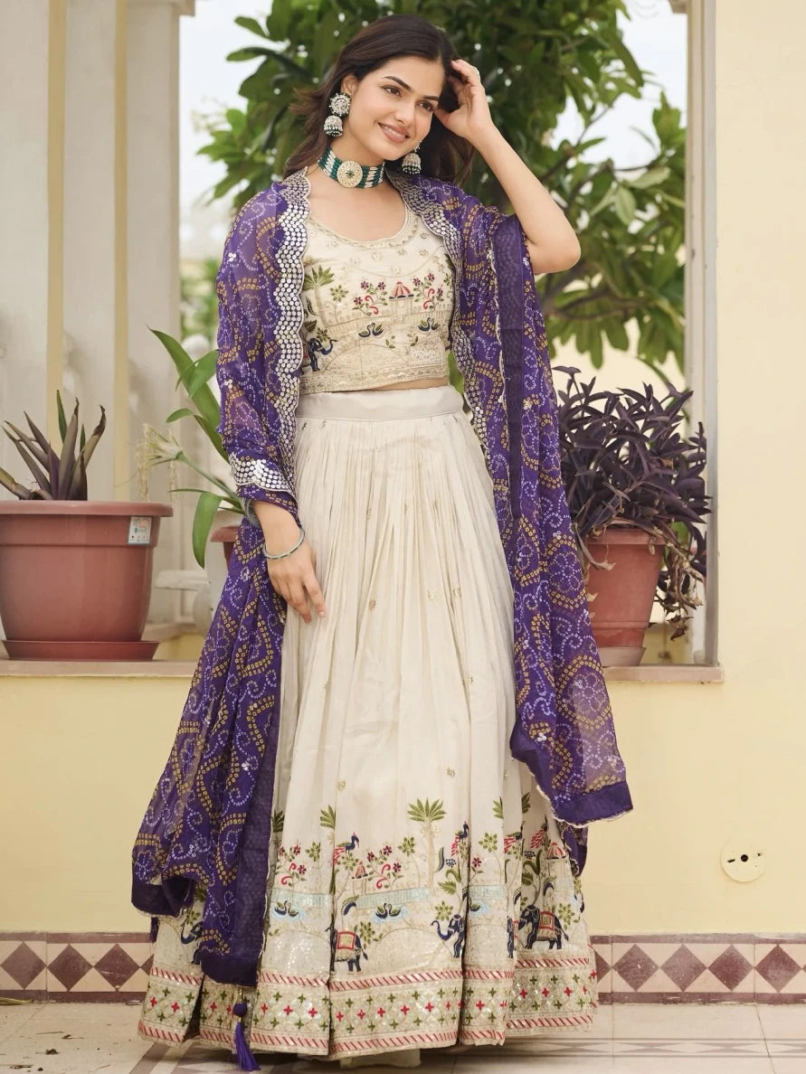 Woman wearing a traditional outfit with a floral design, standing indoors with plants in the background.
