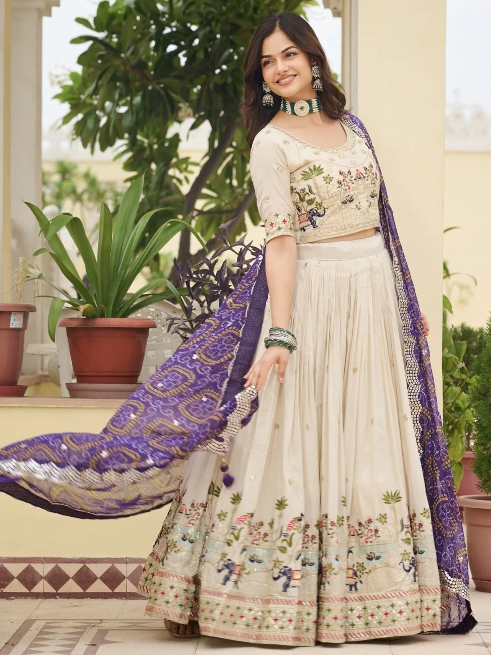 Woman in a traditional outfit with floral patterns and a purple dupatta, standing outdoors.