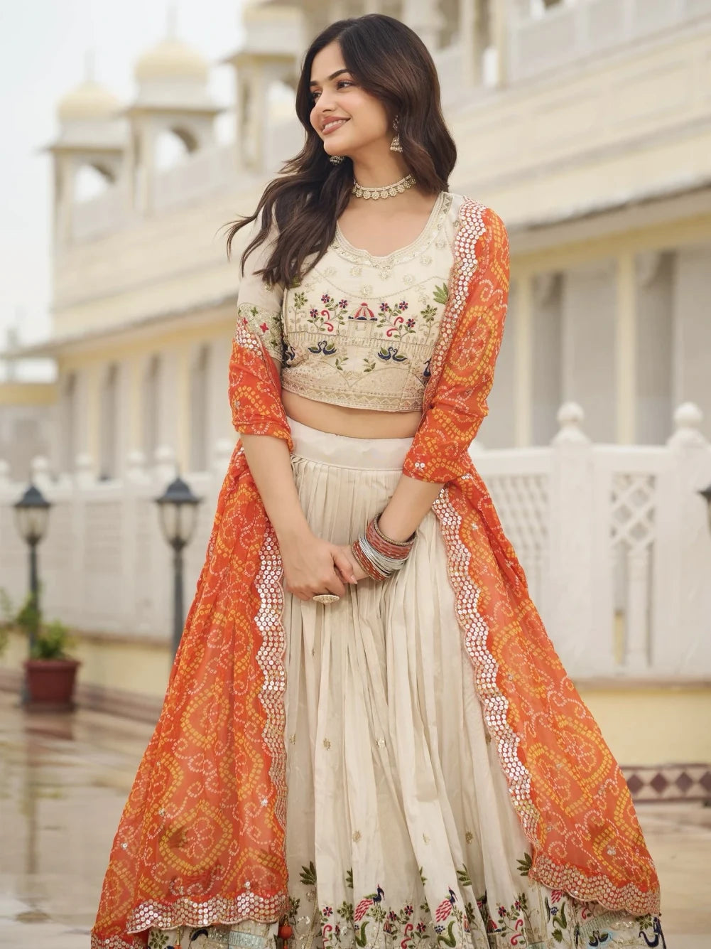 Woman wearing an orange and white traditional outfit with floral patterns in front of a building.