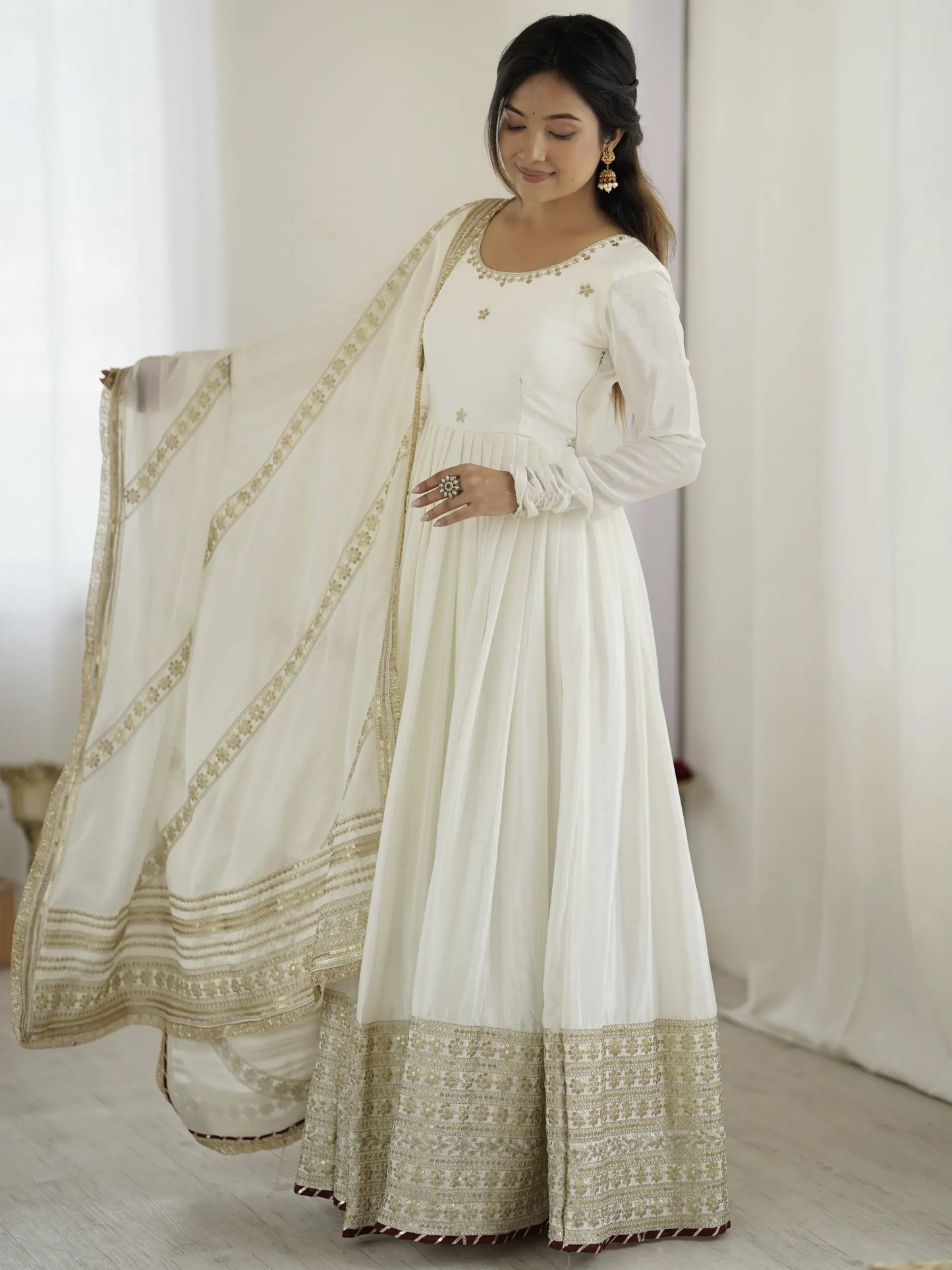 Woman wearing a white traditional outfit with gold embroidery in a minimalistic setting