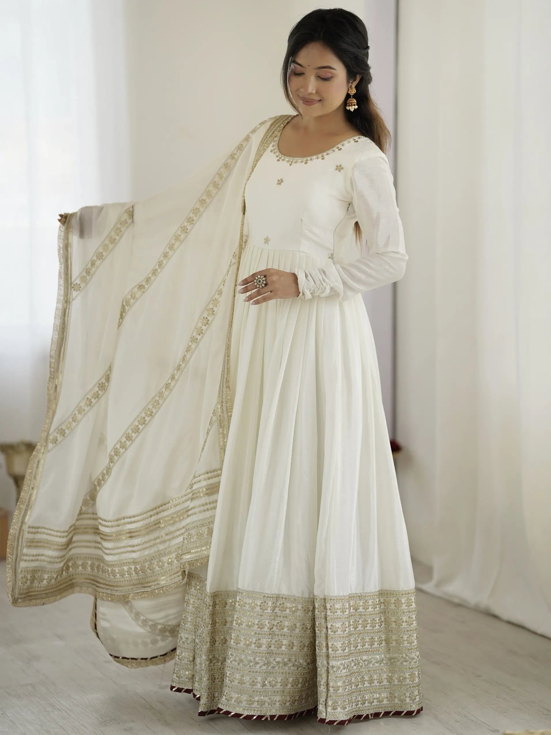 Woman wearing a white traditional outfit with gold embroidery in a minimalistic setting