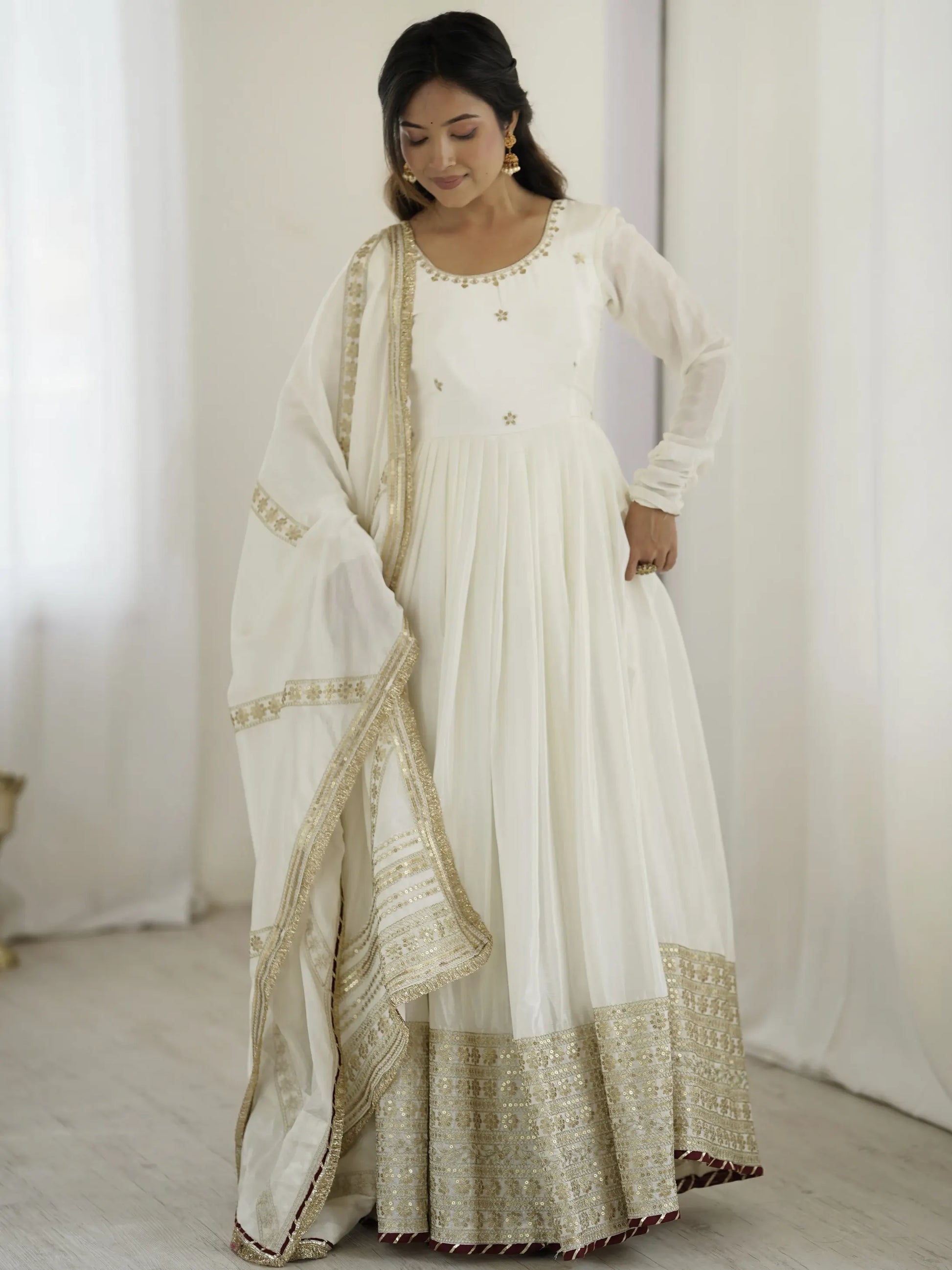 Woman wearing a white traditional outfit with gold embroidery against a white background