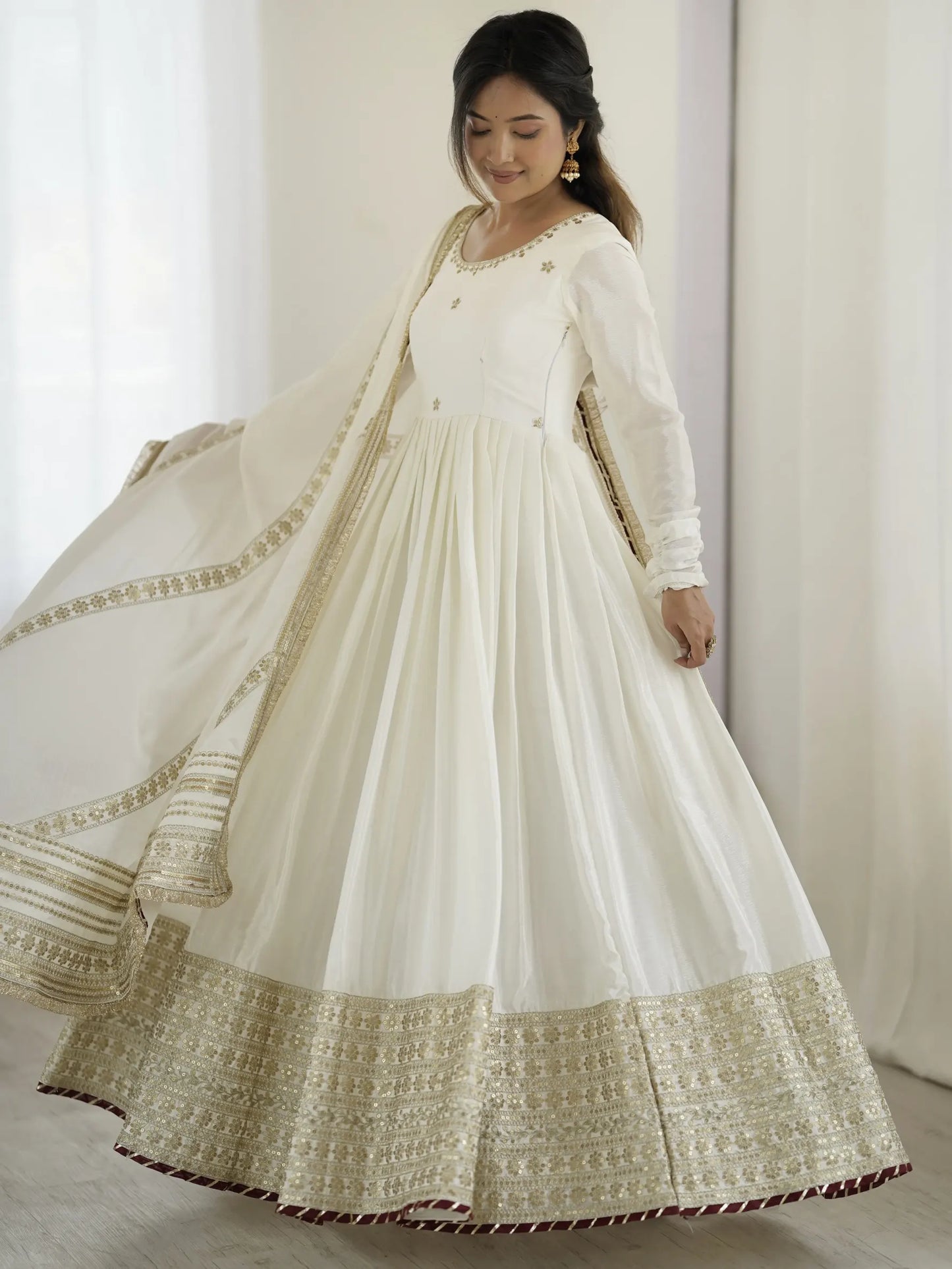 Woman wearing a white traditional outfit with gold embroidery against a white curtain background