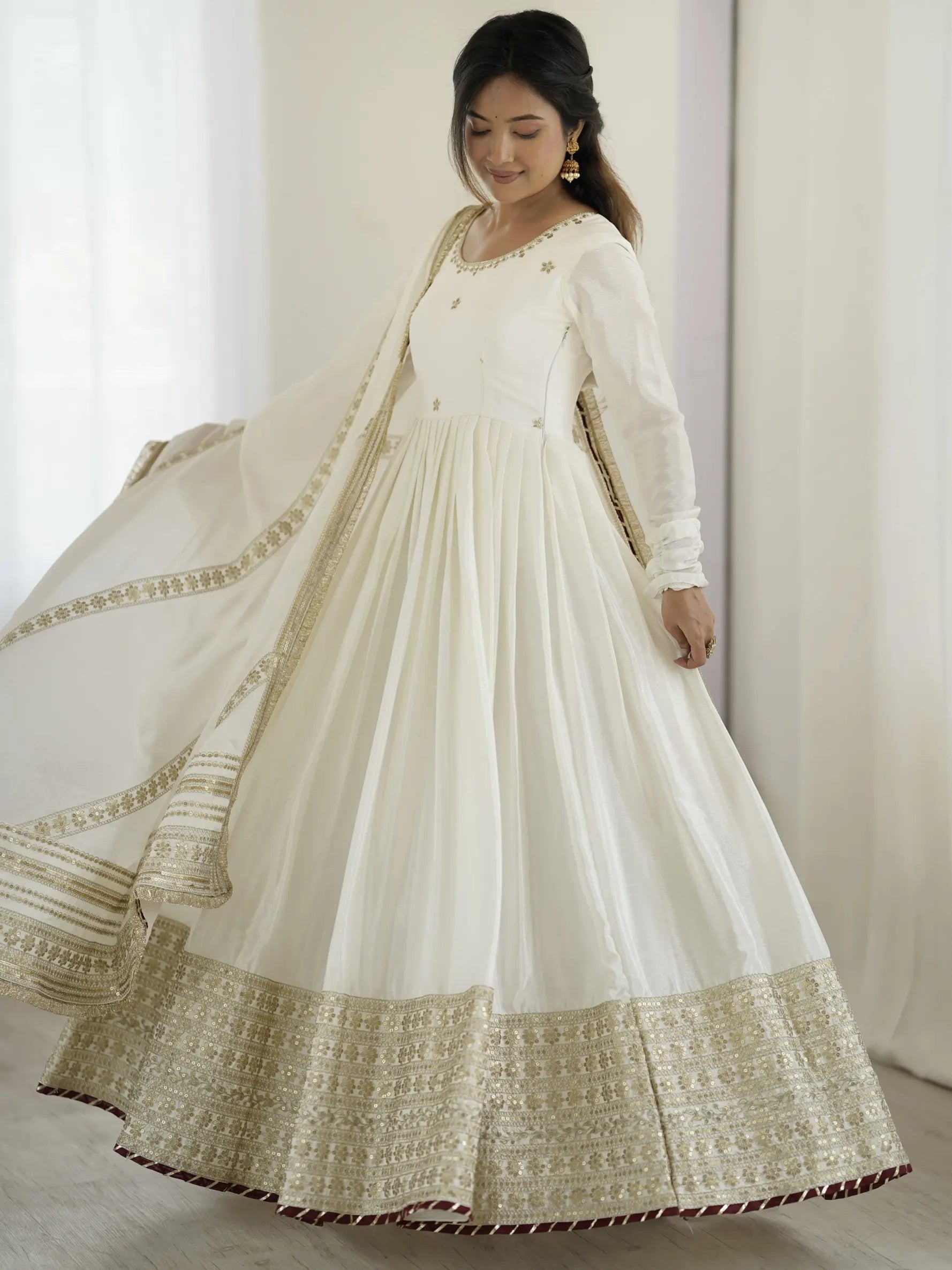 Woman wearing a white traditional outfit with gold embroidery against a white curtain background