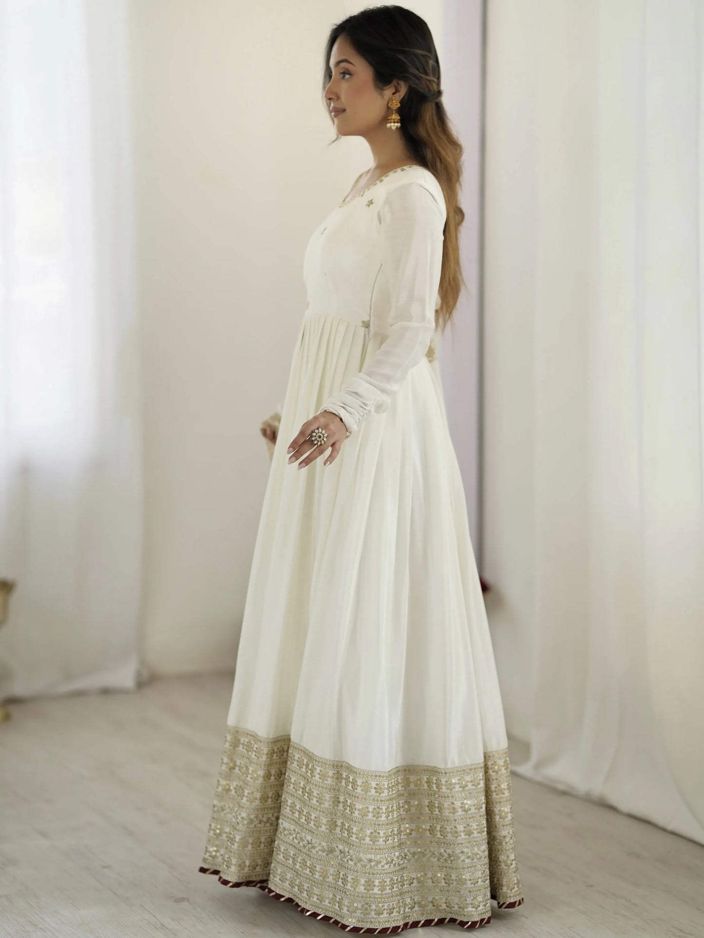 Woman wearing a long white dress with gold embroidery in a minimalistic setting